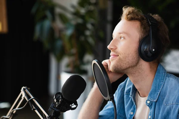 Positive radio host in headphones looking away in podcast studio — Stock Photo