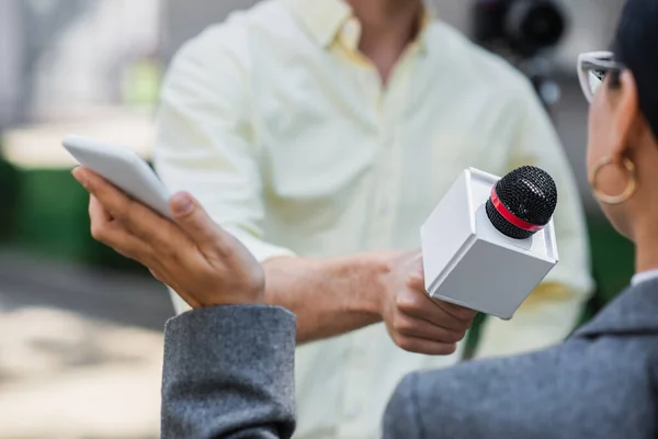 Розмитий репортер тримає мікрофон біля розмитої бізнес-леді зі смартфоном — стокове фото