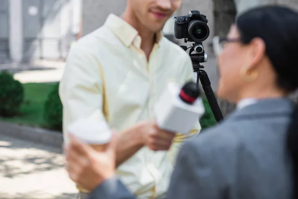 Moderne Digitalkamera auf Stativ in der Nähe verschwommener Reporterin bei Interview mit Geschäftsfrau — Stockfoto