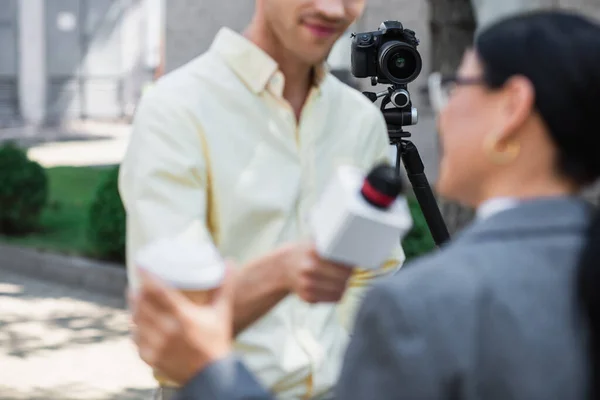 Modern digital camera on tripod near blurred reporter taking interview with businesswoman — Stock Photo