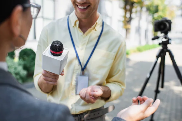 Journaliste joyeux tenant microphone près flou femme d'affaires geste tout en donnant interview — Photo de stock
