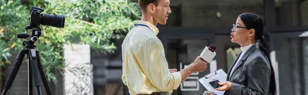 Reporter hält Mikrofon in der Nähe asiatischer Geschäftsfrau mit Brille auf der Straße, Transparent — Stockfoto