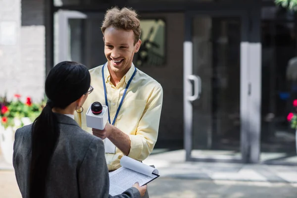 Glückliche Nachrichtensprecherin mit Mikrofon, die Reportagen mit Geschäftsfrau macht — Stockfoto