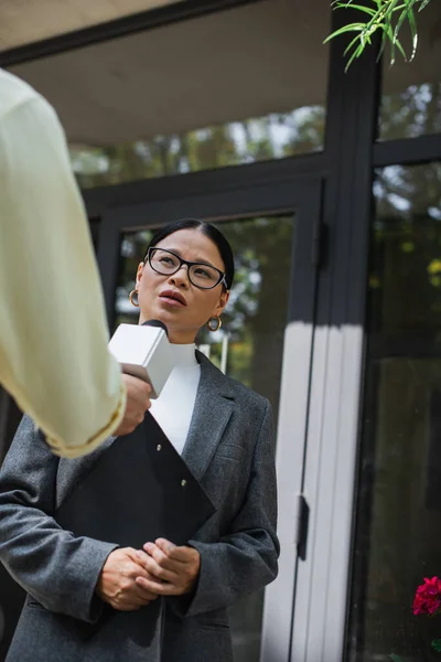 Журналіст тримає мікрофон і бере інтерв'ю азіатській бізнес-леді в окулярах — стокове фото