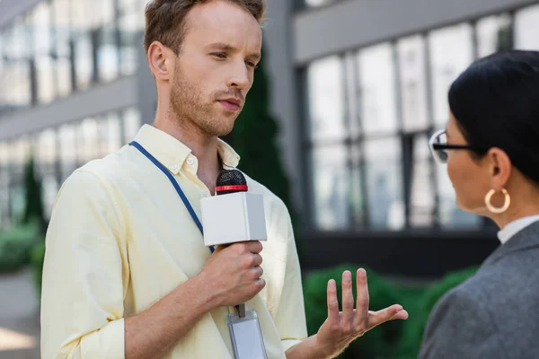 Reporter avec microphone parler avec asiatique femme d'affaires dans lunettes à l'extérieur — Photo de stock