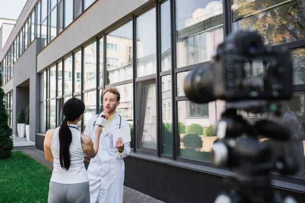 Doctor in white coat holding digital tablet while giving interview to journalist with microphone — Stock Photo