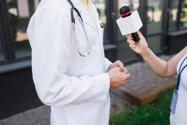 Cropped view of doctor in white coat giving interview to journalist with microphone — Stock Photo