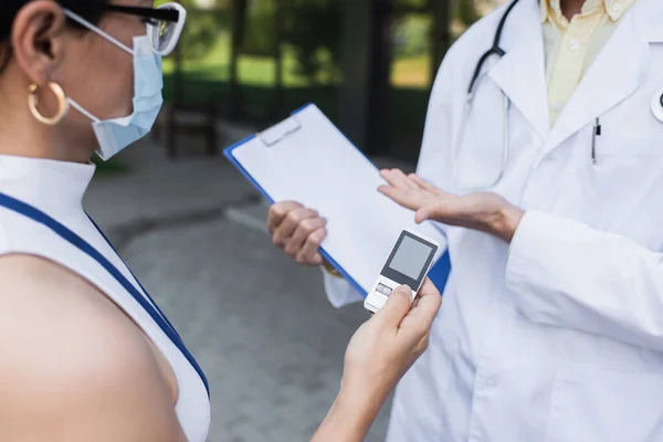 Азіатський репортер в медичній масці тримає диктофон біля лікаря в білому пальто — стокове фото