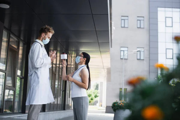 Side view of asian journalist with microphone taking interview of doctor near clinic — Stock Photo
