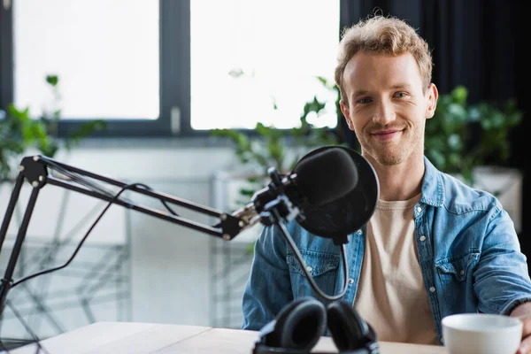 Happy influencer looking at camera near microphone in studio — Stock Photo