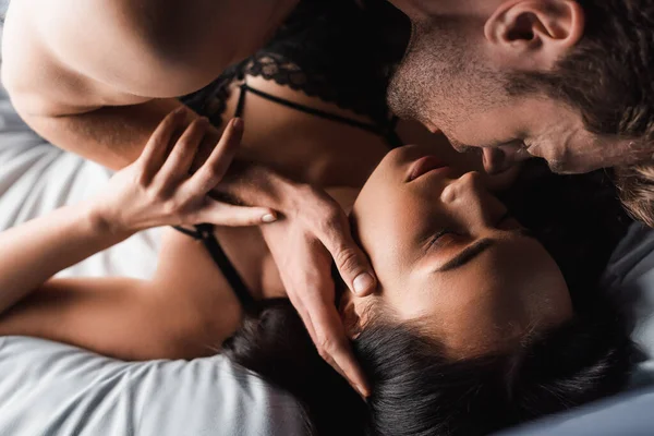 Vista ad alto angolo di uomo senza maglietta baciare fidanzata sensuale in reggiseno sul letto — Foto stock