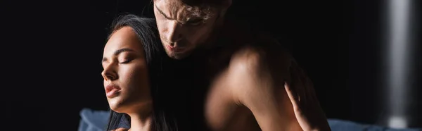 Sensual woman touching muscular boyfriend on black background, banner — Stock Photo