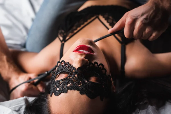 Vue du dessus de la femme en dentelle masque et soutien-gorge couché sur le lit près de copain flou avec fessée pagaie — Photo de stock