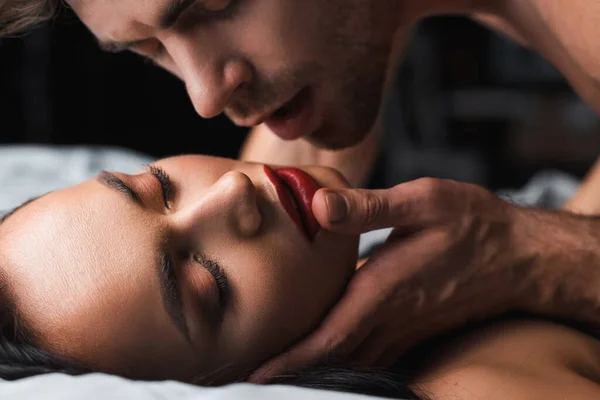 Hombre tocando mujer sexy con los ojos cerrados en la cama sobre fondo negro - foto de stock