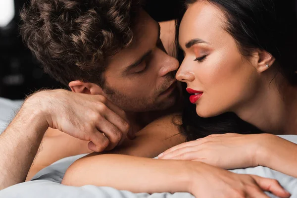 Homme embrasser séduisante petite amie avec des lèvres rouges sur le lit sur fond noir — Photo de stock