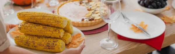 Vue recadrée d'une femme afro-américaine tenant du maïs cuit près d'un dîner festif, bannière — Photo de stock