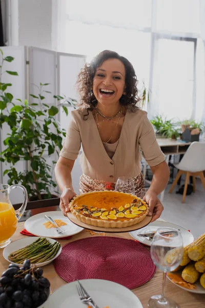 Positive african american woman holding pie near thanksgiving dinner at home — Stock Photo