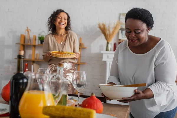 Afroamericano madre tenendo piatto vicino cena del Ringraziamento e figlia offuscata a casa — Foto stock