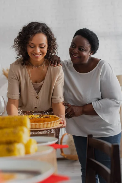 African american woman hugging daughter with tasty pie during thanksgiving celebration — Stock Photo
