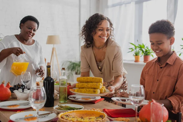 Улыбающаяся африканская американка смотрит на сына рядом с матерью и на ужин в честь Дня Благодарения — стоковое фото