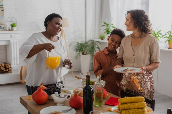 Smiling african american granny pouring orange juice near daughter and grandson during thanksgiving celebration — Stock Photo