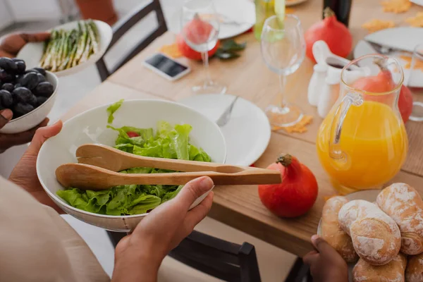 Vista cortada de mulher afro-americana segurando prato com salada perto de mãe turva e comida durante a ação de graças — Fotografia de Stock