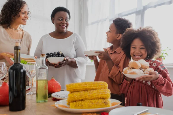 Menina afro-americana segurando pães perto da família e servido jantar de ação de graças — Fotografia de Stock