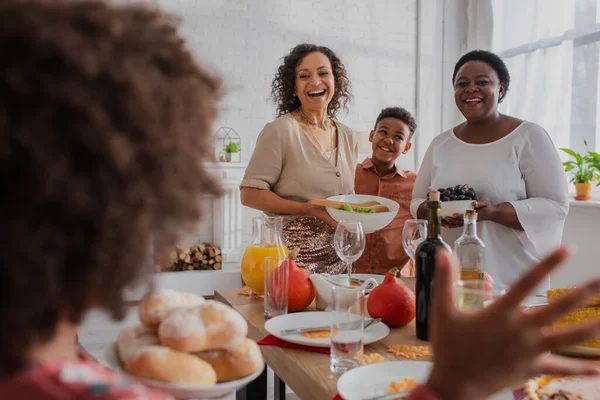 Sorrindo afro-americana família olhando para menina borrada com pães durante a celebração de ação de graças — Fotografia de Stock