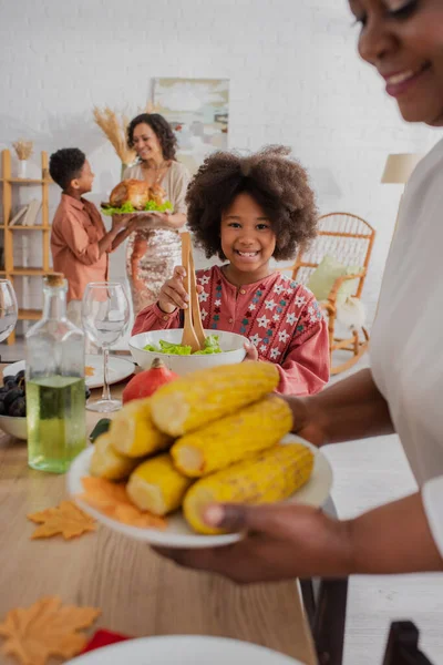 Cheerful african american kid holding salad near blurred granny and thanksgiving dinner — Stock Photo