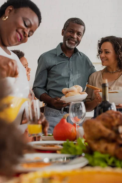 Abuelo afroamericano sosteniendo comida cerca de la familia y cena de acción de gracias - foto de stock