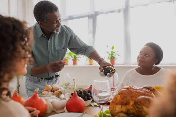Mature african american man pouring wine near family during thanksgiving celebration — Stock Photo