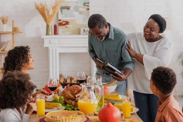 Зрелый африканский американец держит вино рядом с семьей и ужин в честь Дня Благодарения — стоковое фото