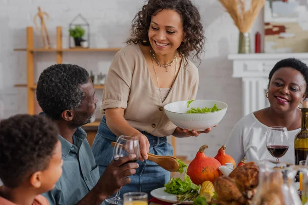 African american woman pouring salad near family and son during thanksgiving celebration — Stock Photo