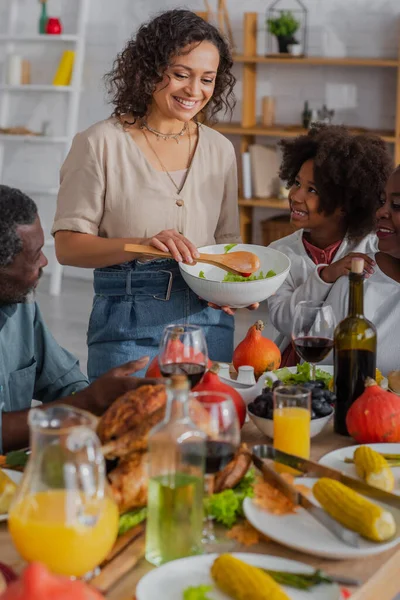 Африканская американская мать держит салат возле улыбающейся семьи и благодарения гиннер — стоковое фото