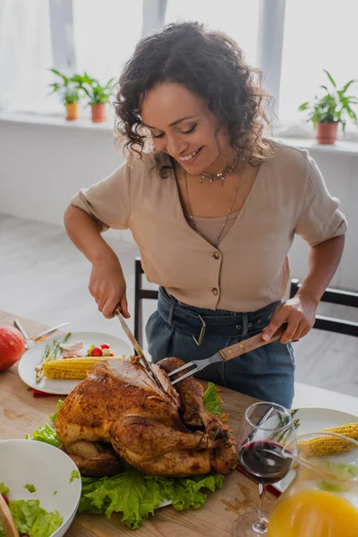 Alegre mujer afroamericana cortando pavo tradicional de acción de gracias - foto de stock