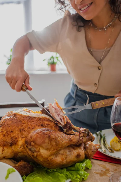 Vista recortada de la borrosa mujer afroamericana cortando delicioso pavo en casa - foto de stock