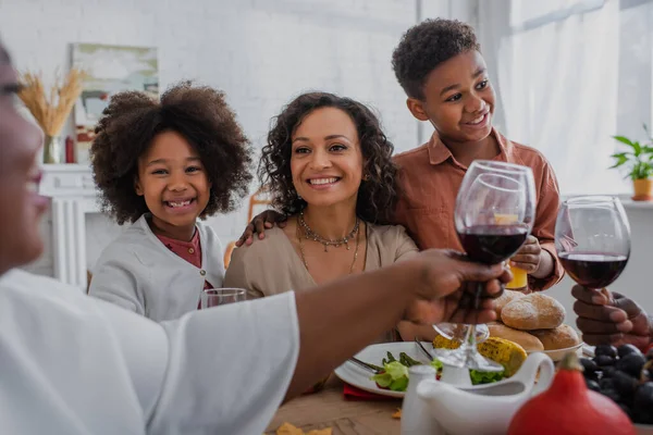 Cheerful african american woman and kids looking at grandparents toasting wine during thanksgiving dinner — Stock Photo