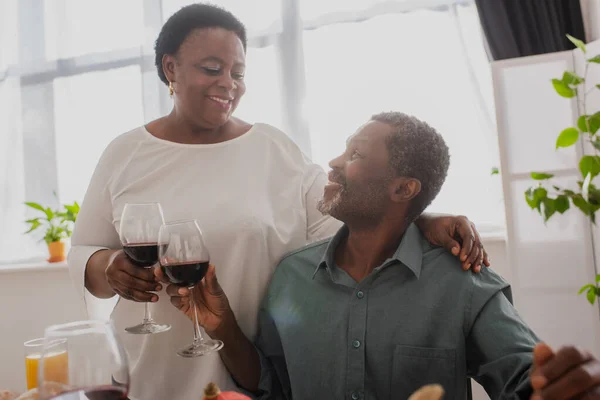 Sonriente pareja afroamericana tostando vino durante la cena de Acción de Gracias - foto de stock