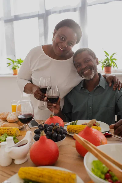 Sonriente mujer afroamericana abrazando marido con vino cerca de la cena de Acción de Gracias - foto de stock