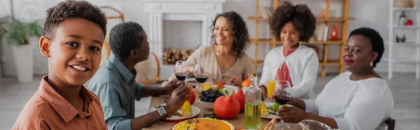 Ragazzo afroamericano sorridente vicino alla famiglia offuscata e ai nonni durante il Ringraziamento, banner — Foto stock