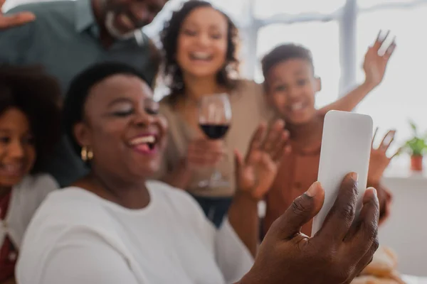Smartphone in mano alla donna afroamericana offuscata che si fa selfie con la famiglia a casa — Foto stock