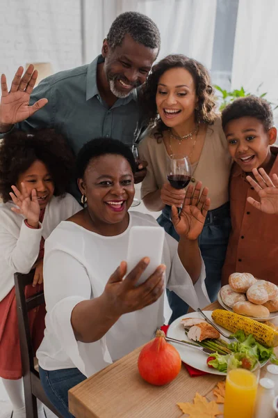 Sorrindo família afro-americana acenando as mãos no smartphone durante a celebração de ação de graças — Fotografia de Stock