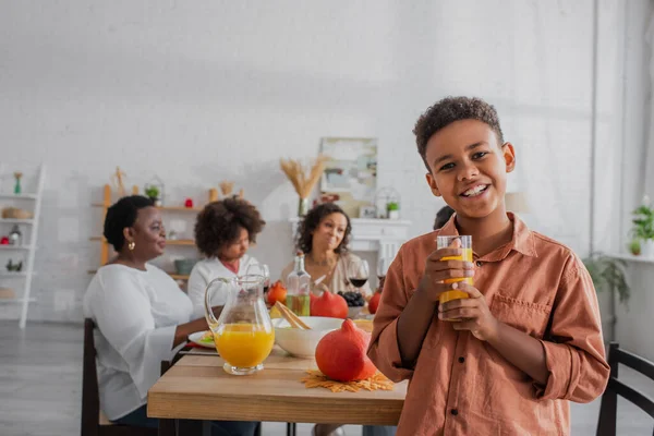 Menino afro-americano segurando suco de laranja perto da família turva durante a ação de graças — Fotografia de Stock