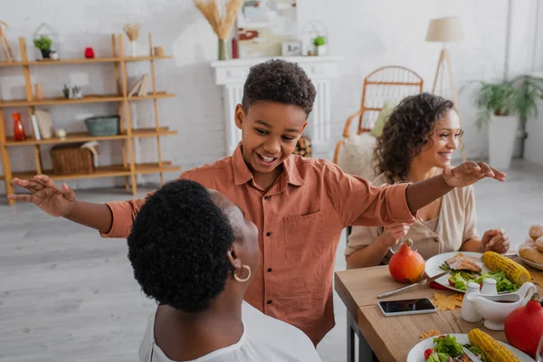 Happy african american boy talking to granny near smiling mother during thanksgiving dinner — Stock Photo