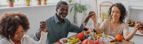 Happy african american family holding hands while praying during thanksgiving dinner, banner — Stock Photo