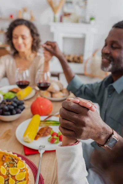 Famille afro-américaine floue tenant la main tout en priant avant le dîner de Thanksgiving — Photo de stock