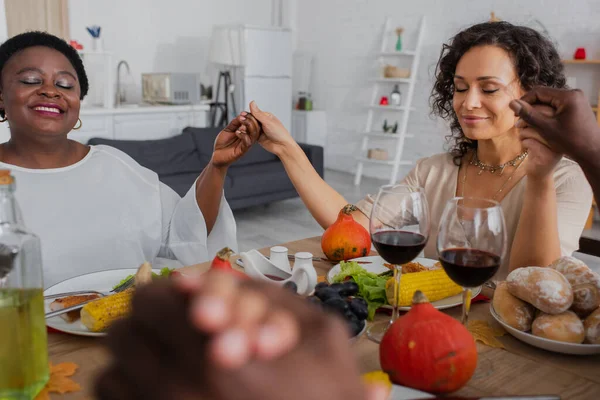 Mujer afroamericana con los ojos cerrados rezando con los padres en la cena de acción de gracias - foto de stock