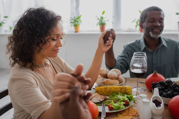 Femme afro-américaine tenant la main avec les parents tout en priant avant le dîner de Thanksgiving avec les yeux fermés — Photo de stock