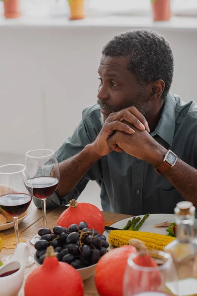 Middle aged african american man sitting with clenched hands at table with thanksgiving dinner — Stock Photo