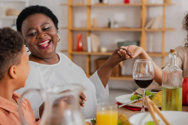 Felice donna afroamericana che prega con nipote e figlia sfocati durante la cena del Ringraziamento — Foto stock